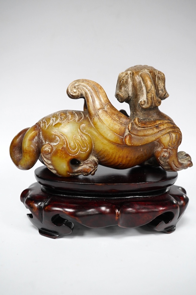 A Chinese archaistic pale celadon russet and burnt jade figure of a winged mythical beast, wood stand, mythical beast 12cm wide. Condition - carving good, stand good